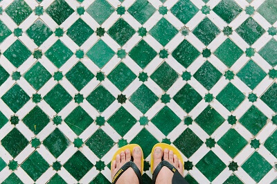 Two feet wearing yellow flip-flops standing on green Moroccan tiles